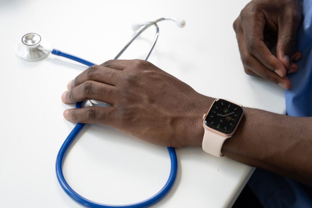 A doctor wearing a watch holds a stethoscope on a table