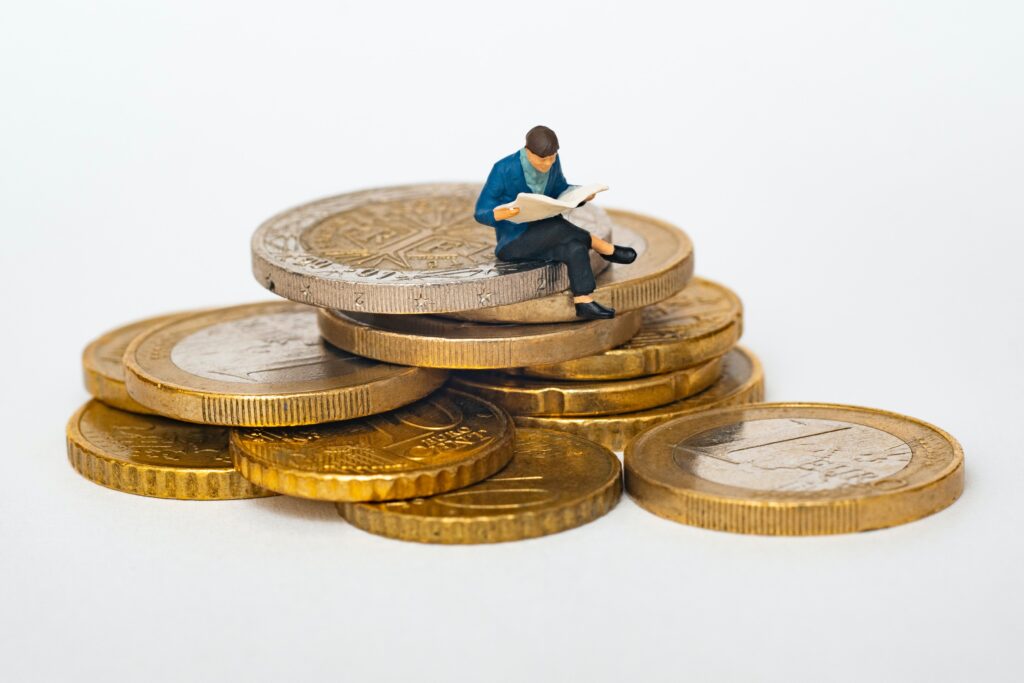 A miniature man sits on a pile of coins