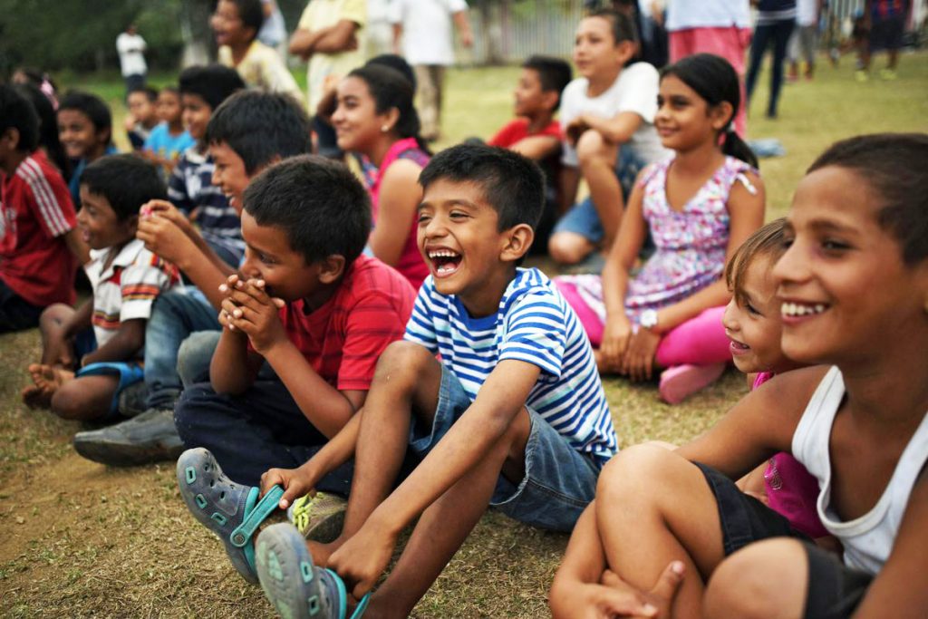 A group of young kids sit on the grass while laughing and smiling